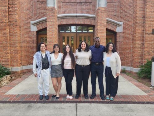 A group of people is posing for a photo in front of a building. They are smiling