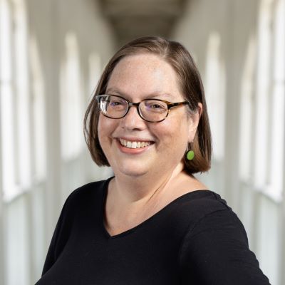 A woman wearing glasses. She is smiling and her headshot is captured indoors against a wall.