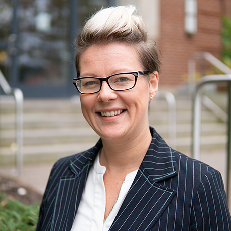 A woman smiling, wearing glasses outdoors